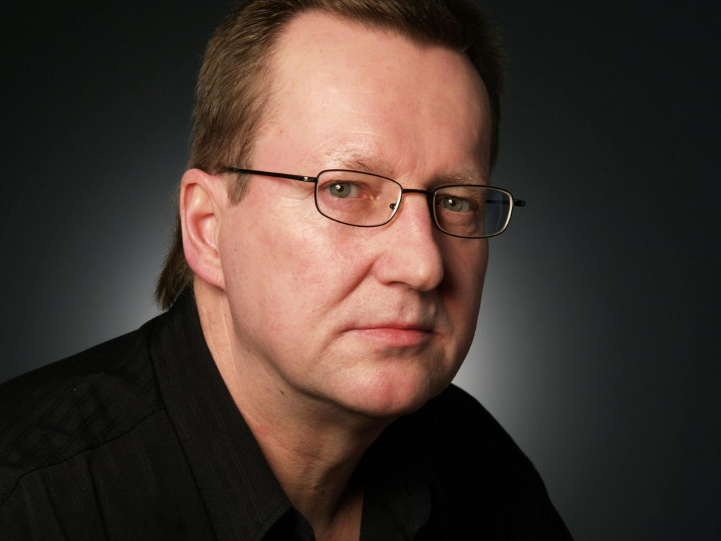 Close-up portrait of a serious businessman in eyeglasses against a dark background.